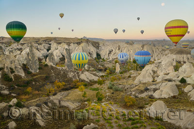 Many hot air balloons over the Red Valley with Uchisar in Cappadocia Turkey at dawn with moon