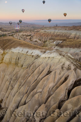 Smooth eroded tuff in the Red Valley of near Goreme Cappadocia Turkey with hot air balloons and moon