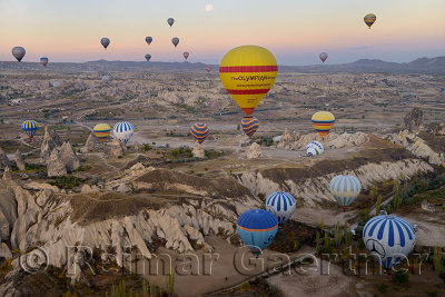 Many hot air balloons over the Red Valley and Goreme Nation Park in Cappadocia Turkey at dawn with moon