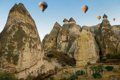 Cave homes in fairy chimneys of Cavusin Cappadocia Turkey with hot air balloons