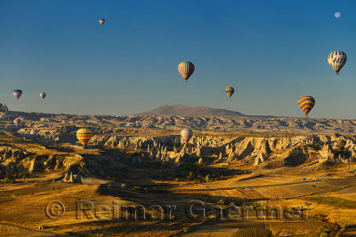 Goreme Love Valley and farm fields Cappadocia Turkey in the morning with hot air balloons and moon