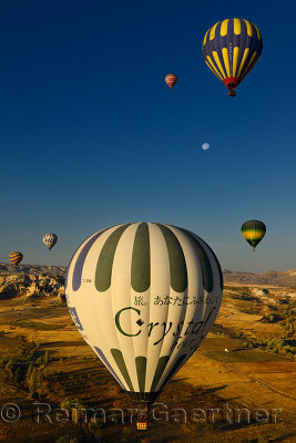 Close up of hot air balloons over farm fields and Love Valley at dawn Cappadocia Turkey with moon