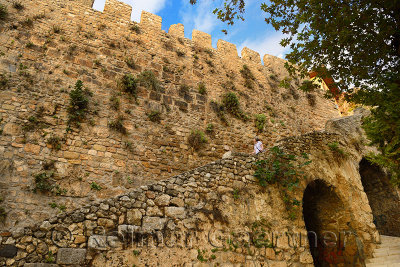 Tourist walking down steps of ancient crenelated Roman stone wall surrounding Antalya harbour Turkey
