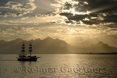 Mediterranean Sea at Antalya harbour Turkey with sunset sunbeams over mountains and tall ship