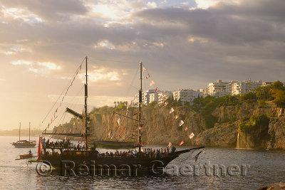 Tall ship entering Antalya Kaleici harbour Turkey at sunset with cliffside waterfalls