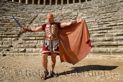 Glowering Roman Gladiator with sword spreading cape in sun on stage at the ancient Aspendos theatre Turkey