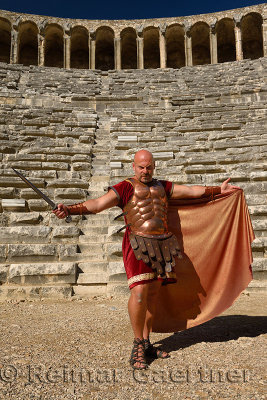 Roman Gladiator with sword spreading cape in sun on stage at the ancient Aspendos theatre Turkey