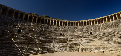 Panorama of semicircular stone seats at ancient Aspendos theatre with upper gallery arches and stage in Turkey