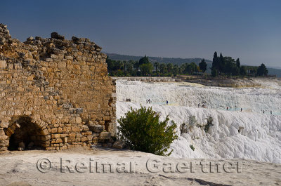 Ancient stone wall of Hierapolis ruins and tourists at thermal waters of Pamukkale Turkey