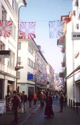 A busy pedestrian shopping street (with flags) in Lucerne.
