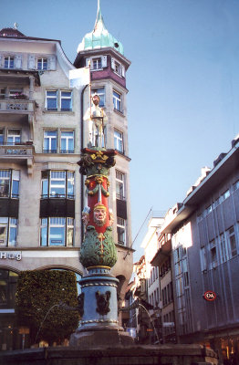 A fountain in the gothic Fritschi style with colorful figures is in the middle of Kapellplatz in Lucerne.