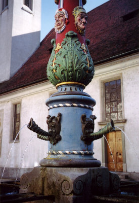 A closer view of the Fritschi-style fountain with water pouring out of spouts of the gothic mask-like faces.