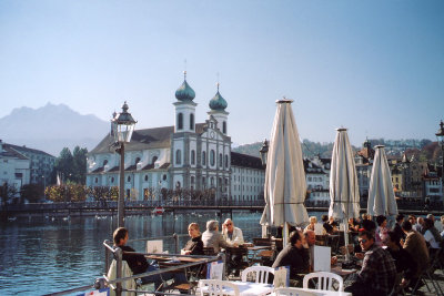 Another view of people having lunch at a cafe on the Reuss River with the Jesuit Church  in the background.