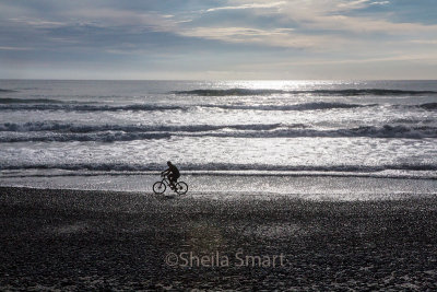 Cyclist on beach with Tasman sea backdrop