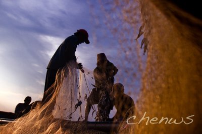 BALI, INDONESIA - JANUARY 16: Fishermen continue to work at dusk, removing their day's catch from the fishing nets on January 16