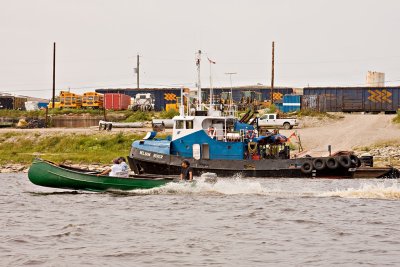 Taxi boat passing docked tug boat in Moosonee with boxcars in background