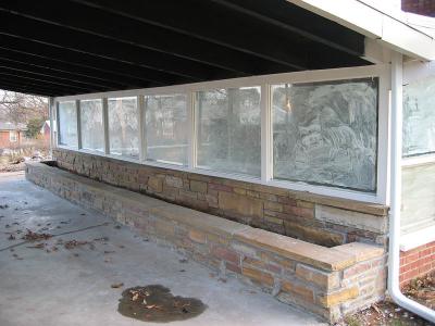 Carport connected to glass room has a built in stone planter.