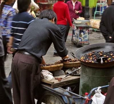 Roasting horse chestnuts outside market. Jishou City, Hunan Province, China