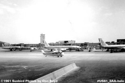 1961 - American DC-7, and two B707s parked on gates while a helicopter taxis out for takeoff