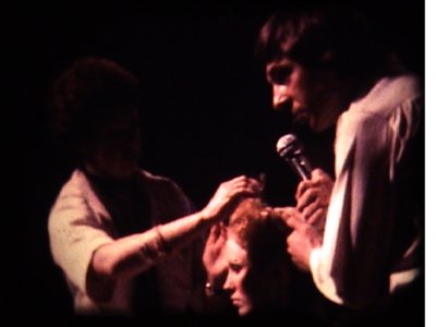 Christopher Brooker commenting and Pat cutting Havington's hair on-stage  Lancaster Gate hotel. 1975