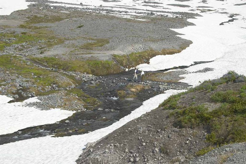 A couple crossing a creek in tennis shoes.