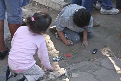These children are playing in the dirt with little cars.  It appears that he is carefully mounding the dirt into a little grave.