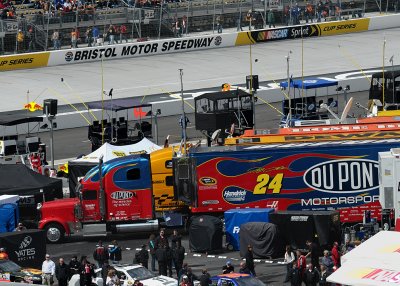 RACE CAR HAULERS PARKED IN THE INFIELD, WITH PIT CREW CHIEF POSITIONS IN THE BACKGROUND