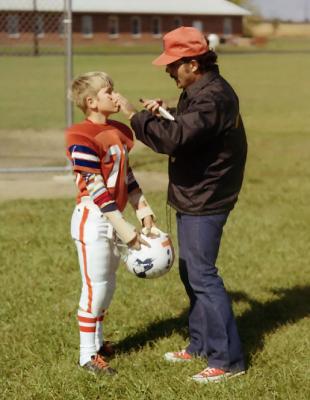 Coach helps boy get ready to play football