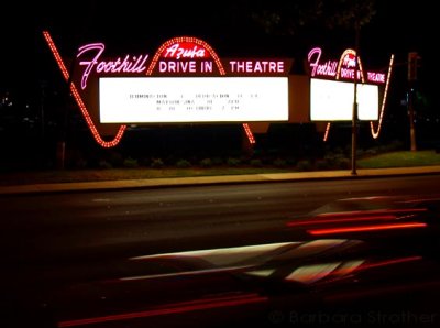 Cars race past the Foothill Drive-In sign on the night of its historic re-illumination. Azusa, California; October 8, 2007. One side features English, the other Spanish.