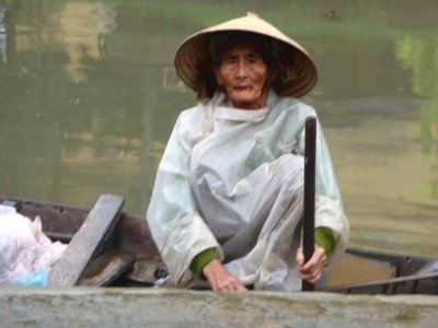 A craggy-faced old woman with rain gear in a rowboat.