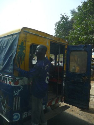 A Senegalese man hanging from the back of a Transport en Commun bus in Dakar.