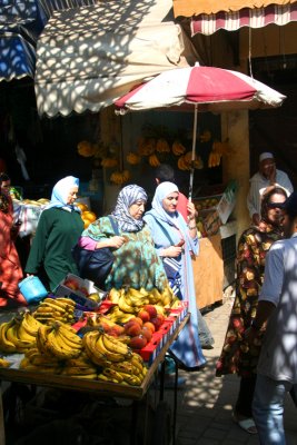 Muslim women walking by a fruit stand in the medina of Fès.