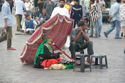 Exotic-looking Moroccan woman sitting in front of a colorful umbrella at Place Djemaa El-Fna.