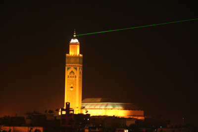 View of the Hassan II Mosque at night with a green spotlight projecting from it.