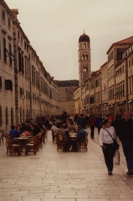Tourists and outdoor cafs on Stradun with the tower of the Church of the Saviour in the background.