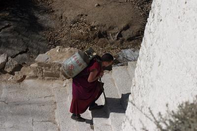 A monk hauling a propane tank up the stairs.