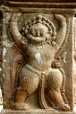 carving of a monster with a human torso, the legs of a garuda, and a lion-like face