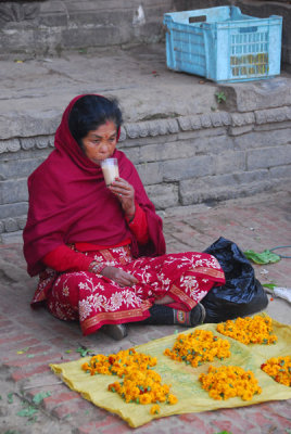 Woman with a glass of hot tea selling flowers, Taumadhi Tole