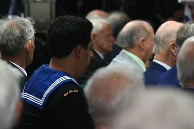 A young NZ Naval Salior sits amongst the older  grey haired veterans