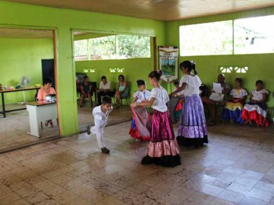 Students dancing at a small, rural school. The teacher is playing music on a boombox. The parents are in the background.