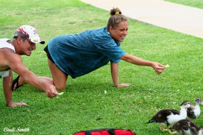 TWO PERFECTLY GOOD ADULTS CRAWLING AROUND ON THE GRASS TRYING TO FEED THE DUCKS BY HAND