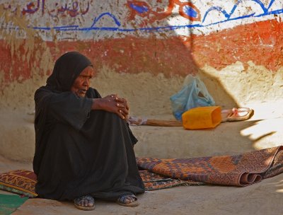 An old Nubian woman sitting in her yard with Arabic letters on the wall ŬǸŮ