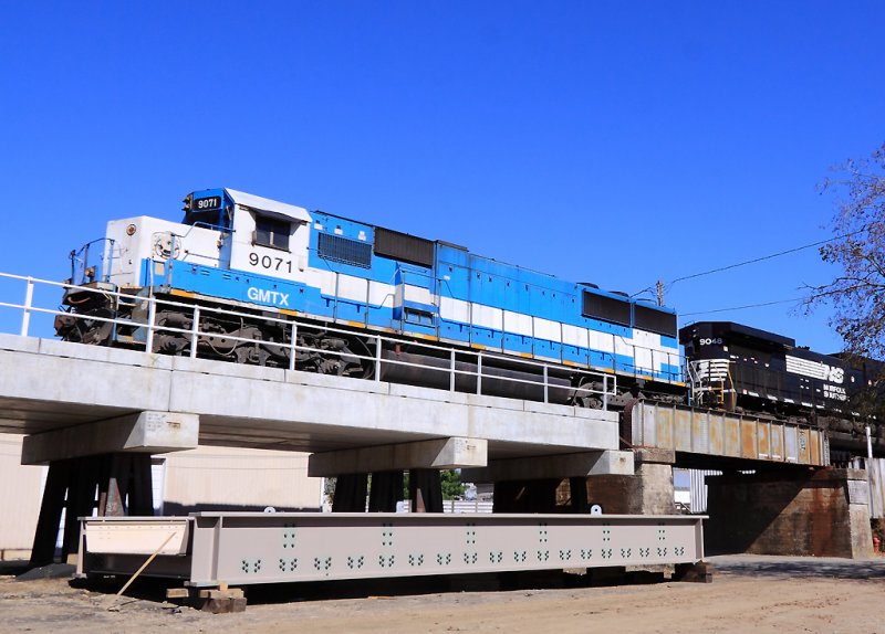 The new bridge span to replaced the old plate girder section lays on the ground, as NS 289 passes 