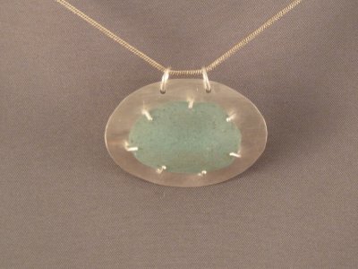 A large piece of aqua beach glass, set on a curved sterling back plate