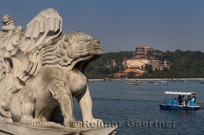 Stone lion on 17 Arch Bridge over Kunming Lake with paddle boaters at Summer Palace Beijing