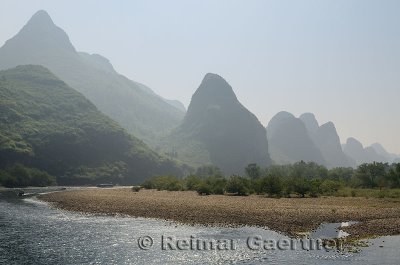 Pebble shore of the Li River with limestone Karst peaks receding into the haze