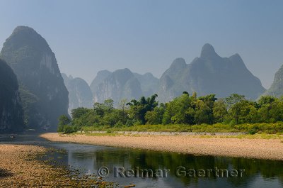Pebble shore of the Li River with limestone Karst cones and peaks in the haze