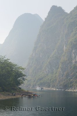 Cruise ship and sightseeing rafts on the hazy Li River in China among the tall karst peaks of Guangxi