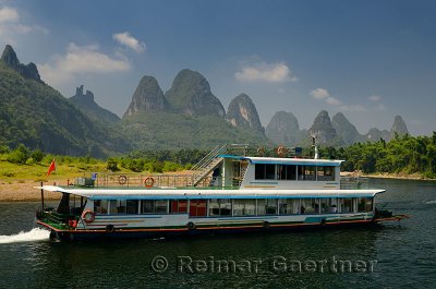 Chinese tour boat cruising down the Li river with bamboo forest and hazy karst peaks