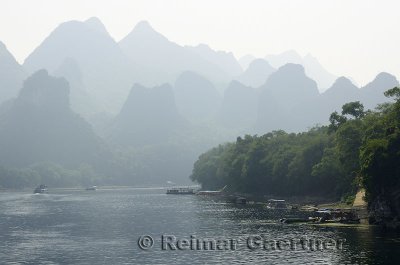 Barges rafts and cruise boats on the Li River Guangxi China with karst dome mountains in the haze